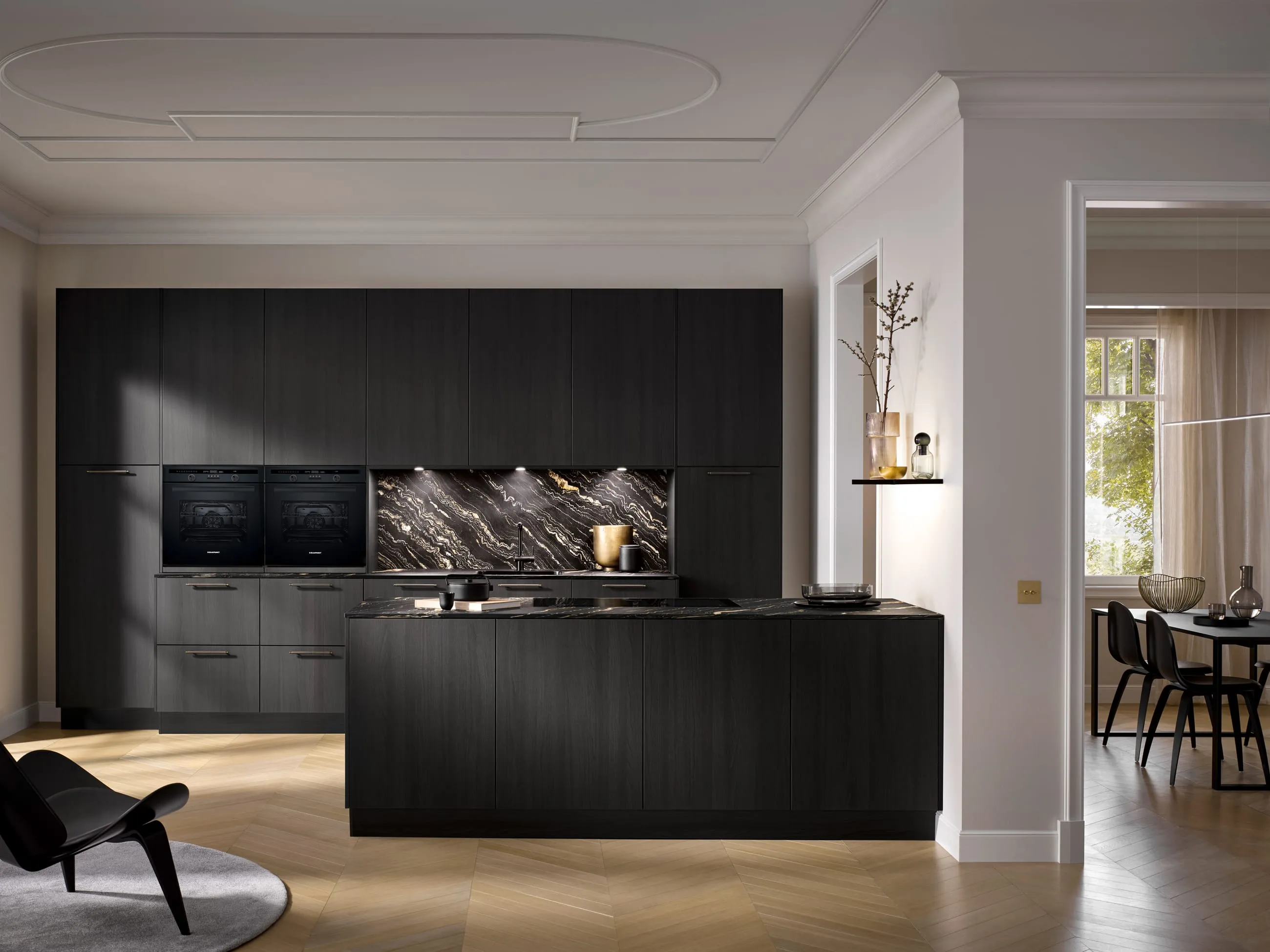 A dark Häcker Systemat kitchen with a veined splashback, in a room with an ornate plaster ceiling